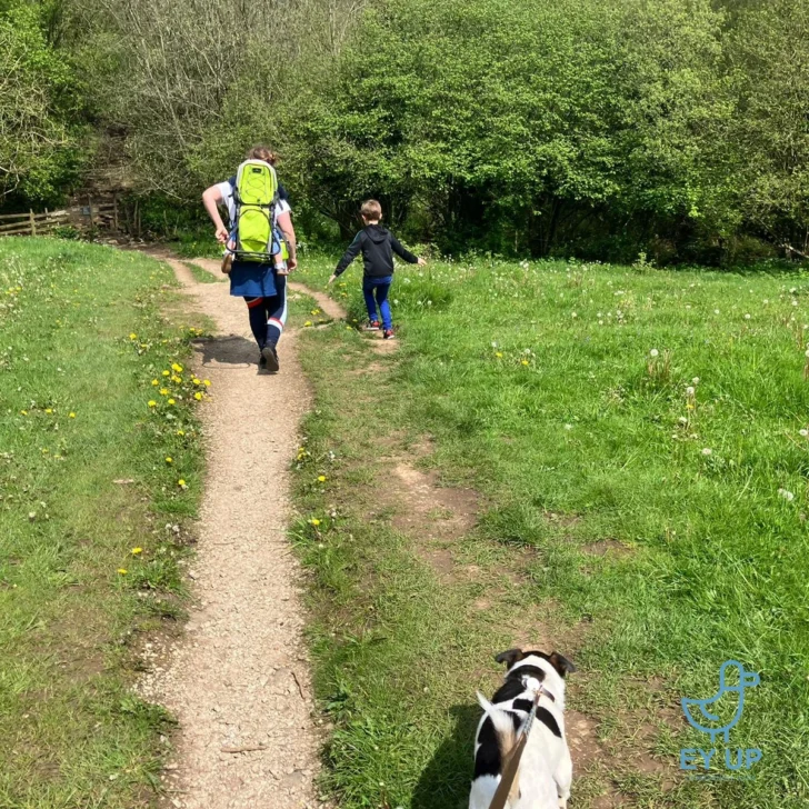 mum with toddler on back and sone and dog walking through holmebrook park